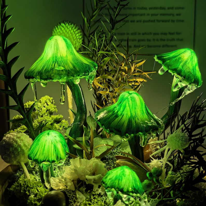Pu&ograve; includere: Un gruppo di sculture di funghi verdi luminosi dall'aspetto vetroso. I funghi sono circondati da varie piante e fiori verdi, creando un'esposizione stravagante e illuminata. I cappelli hanno un effetto strutturato e gocciolante.