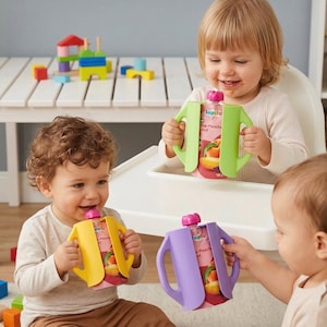 May include: Three young children holding pouches of baby food. Each pouch is in a colorful holder with handles. The pouches have a peach graphic and the text "lupilu". One holder is yellow, one is green, and one is purple.