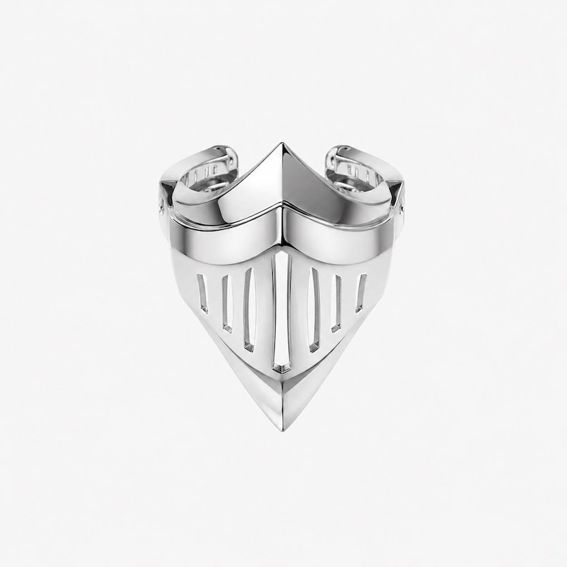 May include: A polished silver-tone ring designed in the shape of a knight's helmet visor. The band features a pointed front section with vertical cutouts resembling a face guard, creating a structured, metallic appearance with a smooth finish.
