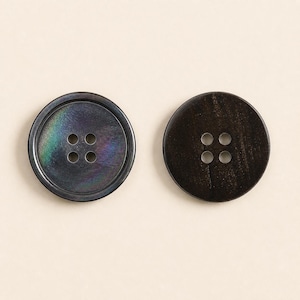 May include: Two round, four-hole buttons. The left button is dark with iridescent, rainbow-like highlights. The right button is a solid, dark brown with a visible wood-grain texture. Both items feature a raised outer rim and a flat center.