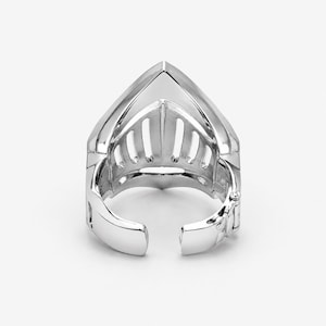 May include: A polished silver-toned ring designed to resemble a medieval knight's helmet visor. The piece features a pointed top, vertical cutouts across the front, and a hinged, open-ended band that allows for adjustment to fit different finger sizes.