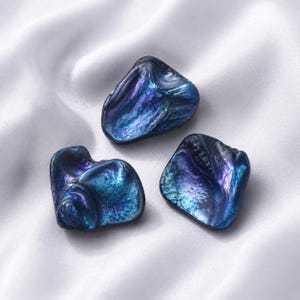 May include: Three irregular, polished shell pieces featuring a deep, iridescent blue and purple finish. Each piece displays a natural, organic shape with a glossy, reflective surface that shifts in color, highlighting the unique texture of the shell.
