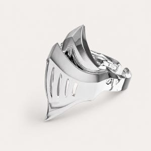 May include: A polished silver-toned ring shaped like a knight's helmet visor. The metal surface is reflective and smooth, featuring a series of vertical cutouts along the front section that mimic the appearance of a medieval armor faceplate.