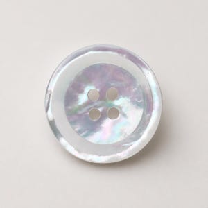 May include: A round, four-hole button crafted from iridescent mother-of-pearl material. The button features a smooth, polished surface with a distinct sheen that displays subtle shifts of white, light purple, and soft blue hues across its face.