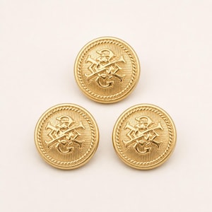 Puede incluir: Tres botones redondos de metal dorado con un diseño de monograma en relieve de las letras G y M entrelazadas en el centro. Cada botón tiene un fondo texturizado con líneas y un borde decorativo de cuerda trenzada alrededor del contorno.