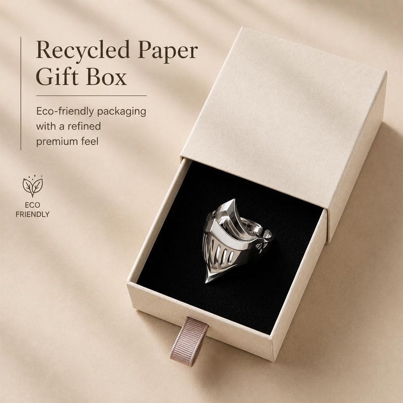 May include: A silver ring shaped like a knight's helmet resting inside a beige recycled paper gift box with a black velvet insert. The box features the text Recycled Paper Gift Box, Eco-friendly packaging with a refined premium feel, and ECO FRIENDLY.