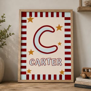 Könnte beinhalten: Gerahmter Kunstdruck mit dem Namen "Carter" und einem großen Buchstaben "C". Der Buchstabe ist hellblau mit dunkelroter Umrandung, umgeben von goldenen Sternen. Der Rand hat rot-hellblaue Streifen.