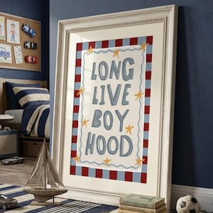 Pode incluir: Uma impressão emoldurada com as palavras "LONG LIVE BOY HOOD" em letras azuis. A moldura é branca com uma borda vermelha e azul. A impressão está no quarto de uma criança com um veleiro de brinquedo e livros.