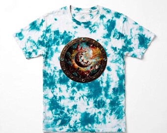 Może przedstawiać: Koszulka z krótkim rękawem w biało-turkusowy wzór tie-dye. Na środku klatki piersiowej znajduje się okrągła grafika przedstawiająca półksiężyc otoczony mgławicą w kolorach pomarańczowym, czerwonym i ciemnym, zamknięta w ozdobnej brązowej ramie.