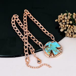 May include: A rose gold chain necklace with a turquoise pendant. The pendant is a square shape with a turquoise stone in the center. The chain is a thick, linked style with a lobster clasp.