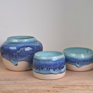 May include: Three ceramic vessels with a blue and white glaze. The largest is a wide, round vase. The other two are smaller, open bowls. The glaze has a dripped effect, with a light blue interior and a darker blue exterior.