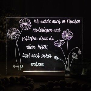 Könnte beinhalten: Leuchtendes Acrylschild mit deutschem Text und floralen Illustrationen. Der Text lautet: "Ich werde mich in Frieden niederlegen und schlafen: denn du allein, HERR, lässt mich sicher wohnen." Psalm 4,9 ist ebenfalls sichtbar.