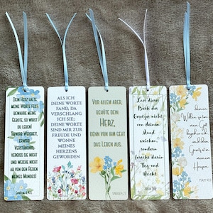 Könnte beinhalten: Fünf rechteckige Lesezeichen aus Papier mit hellblauen Bandquasten an der Oberseite. Jedes Lesezeichen zeigt florale Illustrationen in Blau, Gelb und Grün, gepaart mit deutschen religiösen Texten in verschiedenen Schriftarten.