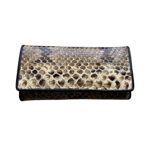 May include: A rectangular clutch wallet featuring a textured snakeskin pattern in shades of beige, brown, and black. The wallet has a flap closure and is finished with a solid black leather trim along the edges, providing a structured appearance.