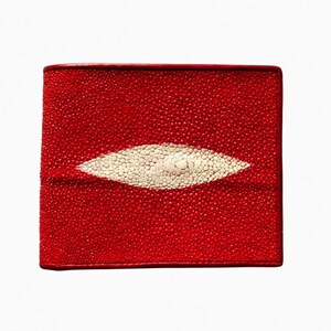 Op de afbeelding: Een rode leren portemonnee met een wit pijlstaartroog-oogontwerp. De portemonnee is rechthoekig met afgeronde hoeken en een getextureerd oppervlak. Het witte ontwerp is ovaal van vorm en gecentreerd.