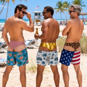 Può includere: Tre paia di costumi da bagno indossati su una spiaggia. Il primo paio presenta una stampa floreale tropicale blu con una fascia in vita a righe rosse e bianche. Il secondo paio ha una base bianca con stampe di furgoni da surf blu e una fascia in vita dorata. Il terzo paio mostra un motivo a stelle blu e strisce rosse con una fascia in vita leopardata.