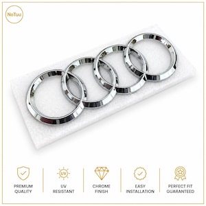 May include: A chrome-finished emblem featuring four interlocking rings, presented on a rectangular white foam block. Below the emblem, five icons are displayed with the text: PREMIUM QUALITY, UV RESISTANT, CHROME FINISH, EASY INSTALLATION, PERFECT FIT GUARANTEED.