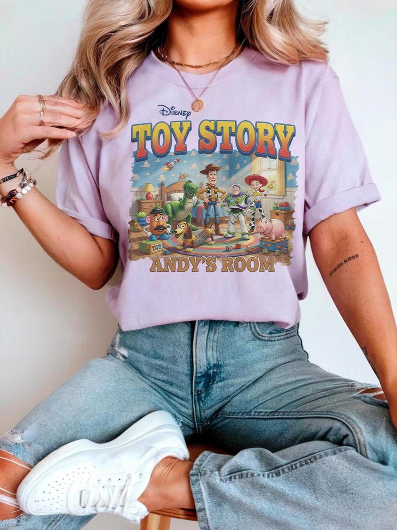 Puede incluir: Una camiseta de color lila con el logotipo y los personajes de Disney Toy Story. El gr&aacute;fico incluye a Woody, Buzz Lightyear y otros personajes en la habitaci&oacute;n de Andy. El texto "ANDY'S ROOM" est&aacute; impreso debajo.
