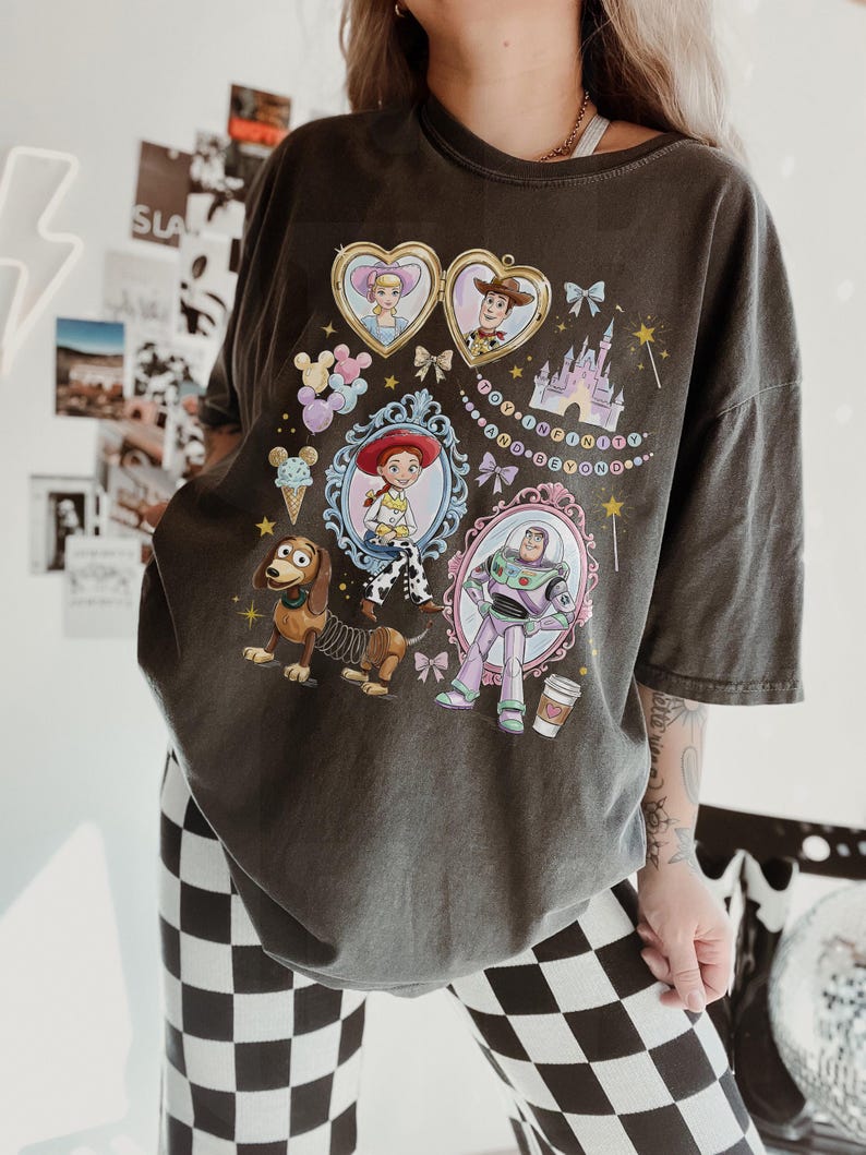 May include: Dark grey t-shirt with a colourful graphic of Toy Story characters in ornate frames. The design includes images of Woody, Buzz Lightyear, and other characters, with the phrase "To infinity and beyond".