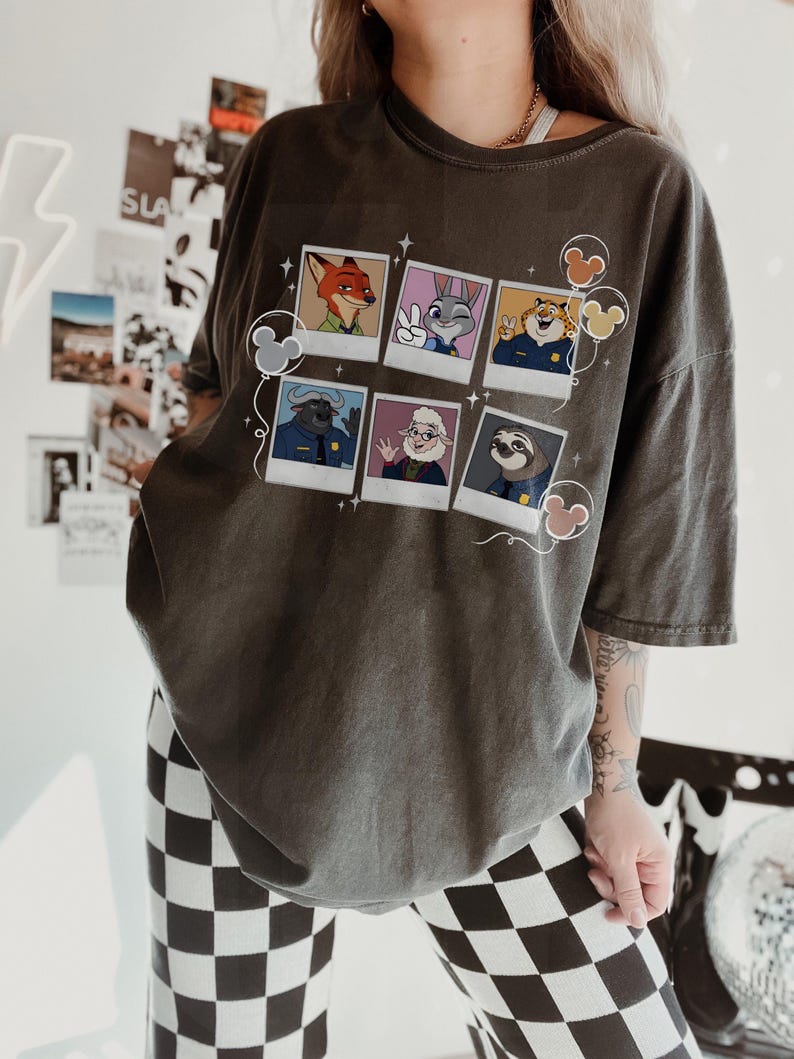 May include: Dark gray t-shirt featuring a collage of cartoon character portraits. The portraits include a fox, a rabbit, a tiger, a buffalo, a sheep, and a sloth. Mickey Mouse-shaped balloons and stars decorate the design.