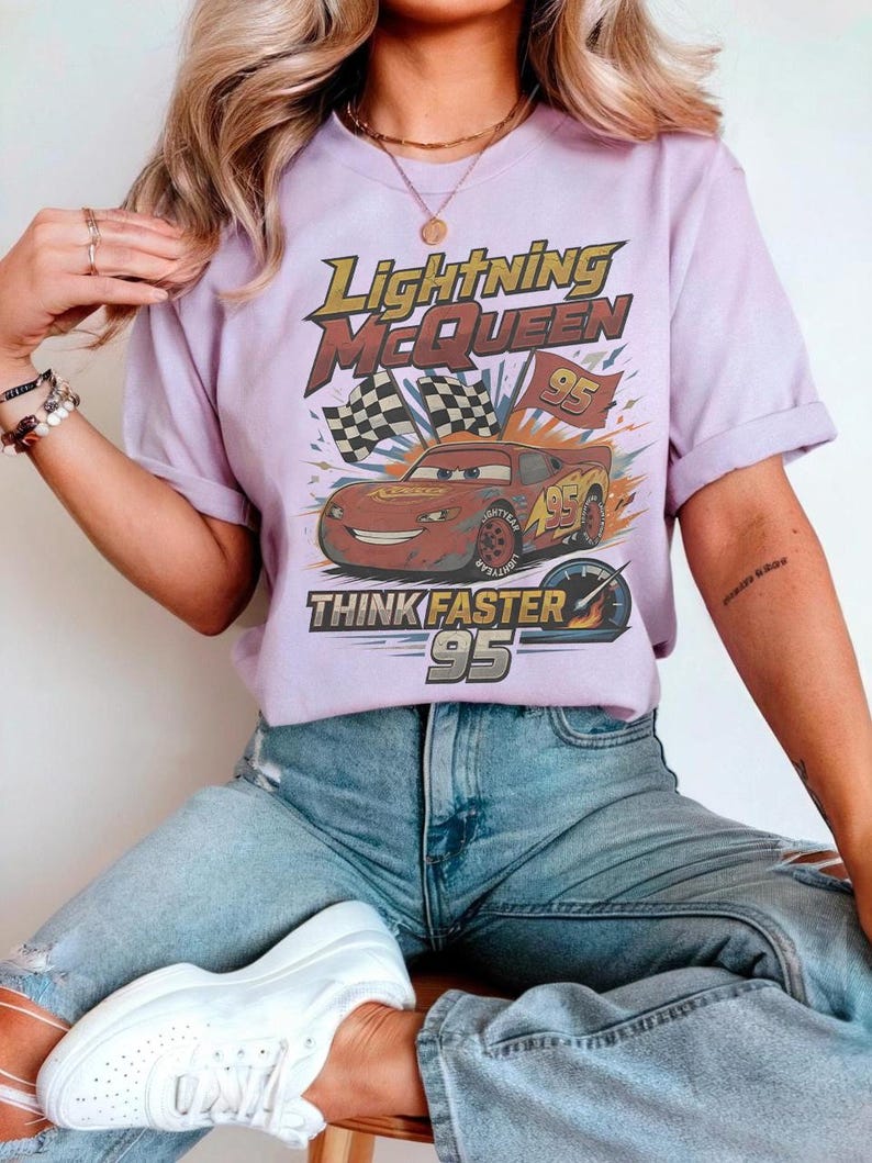 Pode incluir: Uma camiseta lil&aacute;s com um gr&aacute;fico de Rel&acirc;mpago McQueen do filme Carros. O design inclui o texto "Lightning McQueen", "95" e "Think Faster". A camisa &eacute; usada com jeans azul.