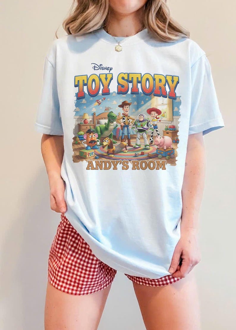 Puede incluir: Camiseta azul claro con el logotipo de Disney Toy Story y personajes. El gr&aacute;fico incluye a Woody, Buzz Lightyear y otros personajes en la habitaci&oacute;n de Andy. La camiseta se combina con pantalones cortos a cuadros rojos y blancos.