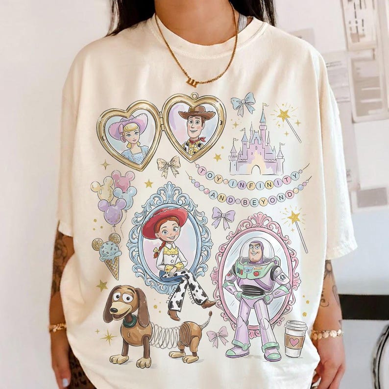 May include: Cream-coloured t-shirt featuring cartoon illustrations of characters from the movie Toy Story. The design includes portraits of Woody, Buzz Lightyear, Jessie, and others, along with the text "TO INFINITY AND BEYOND".
