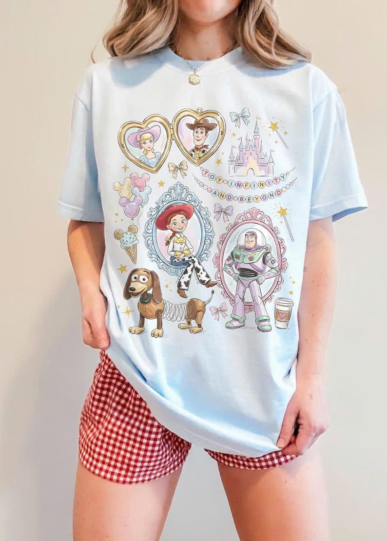 May include: Pale blue t-shirt with Toy Story cartoon characters. The design includes Woody, Buzz Lightyear, Jessie, and other characters in ornate frames, with the phrase "TO INFINITY AND BEYOND".