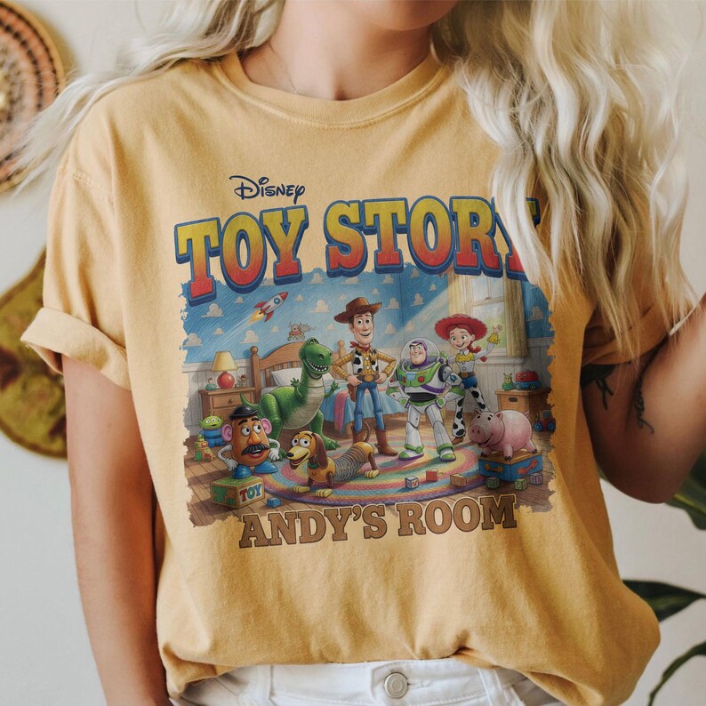 Puede incluir: Camiseta de color amarillo mostaza con un gr&aacute;fico de la pel&iacute;cula de Disney Toy Story. El gr&aacute;fico incluye las palabras "TOY STORY" y "ANDY'S ROOM" con im&aacute;genes de Woody, Buzz Lightyear y otros personajes.