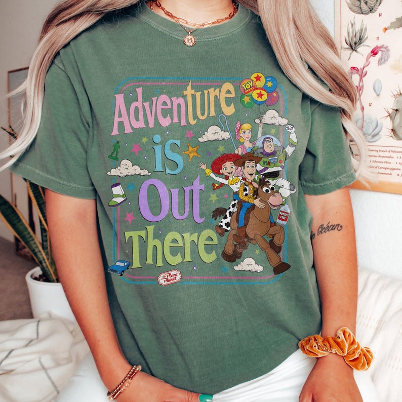 Pode incluir: Camiseta verde com a frase "Adventure is Out There" em um design retr&ocirc; colorido. O gr&aacute;fico apresenta personagens do filme Toy Story, incluindo Woody, Buzz Lightyear e Jessie. Um design divertido para os f&atilde;s do filme de anima&ccedil;&atilde;o.