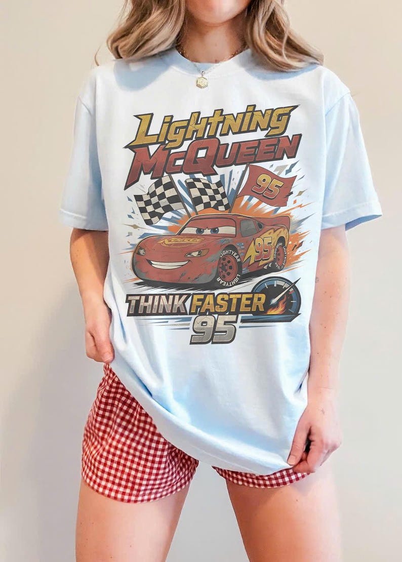 Pode incluir: Camiseta azul clara com Lightning McQueen do filme Carros. O design inclui o texto "Lightning McQueen", "Think Faster" e o n&uacute;mero "95". Apresenta tamb&eacute;m uma bandeira quadriculada e um veloc&iacute;metro.