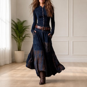 May include: A long-sleeved navy blue button-down top paired with a matching floor-length skirt featuring a mix of solid navy fabric and plaid panels. The outfit is cinched at the waist with a wide brown leather belt and worn with brown boots.