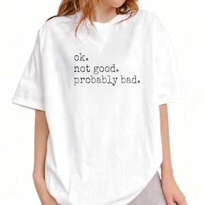 May include: White t-shirt with the text "ok. not good. probably bad." in a simple, black font. The shirt has short sleeves and a relaxed fit. The overall style is casual and comfortable.