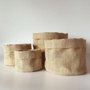 Może przedstawiać: Biały ceramiczny kubek z czarnym uchwytem i napisem "But First, Coffee" czarną, odręczną czcionką. Kubek stoi na białej powierzchni.