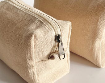 Op de afbeelding: Twee beige canvas etuis met ritssluiting in verschillende maten. De kleinere etui staat op de voorgrond, met een zichtbare ritssluiting en een YKK ritstrekker. De grotere etui staat op de achtergrond. Beide etuis zijn gemaakt van een textuurstof.