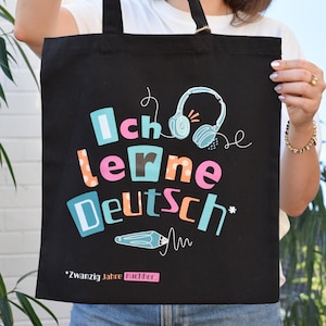 Puede incluir: Una bolsa de tela negra con el texto colorido Ich lerne Deutsch, un gráfico de auriculares azul claro y un icono de lápiz. Debajo del diseño principal, el texto dice Zwanzig Jahre nachher en blanco y naranja con un acento rectangular rosa.
