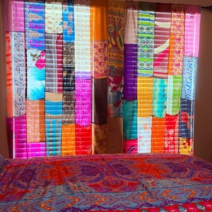 Pode incluir: Um par de cortinas feito de tiras verticais de tecido multicolorido com vários padrões florais, geométricos e abstratos. As cortinas estão penduradas num varão e exibem uma gama vibrante de cores, incluindo rosa, laranja, azul e amarelo.