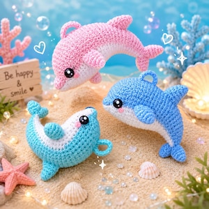 Peut inclure: Trois dauphins en crochet de couleur rose, bleu clair et bleu moyen avec le ventre blanc. Chaque dauphin possède de grands yeux noirs, des joues roses et une petite boucle sur la nageoire dorsale. Un panneau en bois indique Be happy & smile.