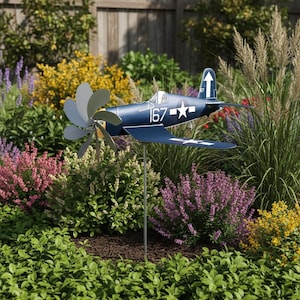 May include: A navy blue metal airplane yard spinner with a propeller and the number 167 on the side. The airplane has white stars and a white arrow on the tail. The yard decoration is in a garden with colorful flowers and greenery.