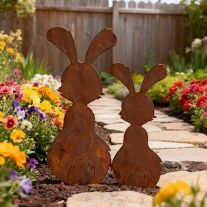 May include: Two rusty metal rabbit yard art pieces. The larger rabbit is approximately 3 feet tall, and the smaller one is about 2 feet tall. They are placed in a garden with colorful flowers and a stone pathway.
