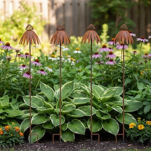 May include: Four rusty metal garden stakes with a flower-like design. The stakes are placed in a garden bed filled with green plants and purple and white flowers. The stakes have a decorative, umbrella-shaped top.