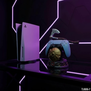 以下が含まれることがあります： 白と黒のゲーム機、水色のコントローラー、装飾用の斧。 コントローラーは、金とブロンズのアクセントが付いた詳細なベースに置かれています。 背景には、幾何学的なネオンパープルの照明があります。