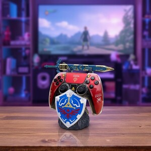 Könnte beinhalten: Ein rot-schwarzer Videospiel-Controller-Ständer mit Schwert- und Schild-Design. Der Ständer trägt den Text "ZEON" und ein blaues und goldenes Schwert, das oben aufliegt. Ein blau-weißer Schild befindet sich davor.
