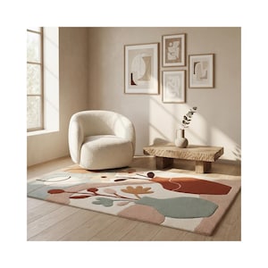 May include: A cozy living room scene featuring a cream-colored, rounded armchair, a wooden coffee table, and a patterned rug with abstract floral and vase designs in muted colors. Artwork hangs on the wall, and a vase with greenery sits on the table.