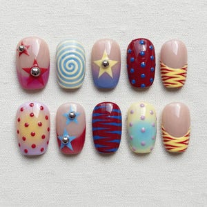 Puede incluir: Un conjunto de diez uñas postizas con varios diseños. Los diseños incluyen estrellas, espirales, puntos y rayas en colores como rojo, azul, amarillo y rosa. Algunas uñas tienen adornos plateados.