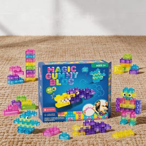 May include: A box of "Magic Gummy Bloc" building blocks with 40 pieces. The blocks are colorful and translucent, in shades of pink, yellow, green, blue, and purple. The box features a cartoon alligator and robot made of blocks.