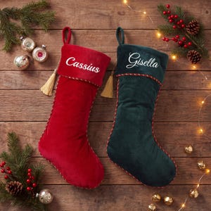 May include: A red velvet Christmas stocking with the name Cassius embroidered in white and a dark green velvet Christmas stocking with the name Gisella embroidered in white, both featuring a hanging loop and a decorative twisted cord trim.