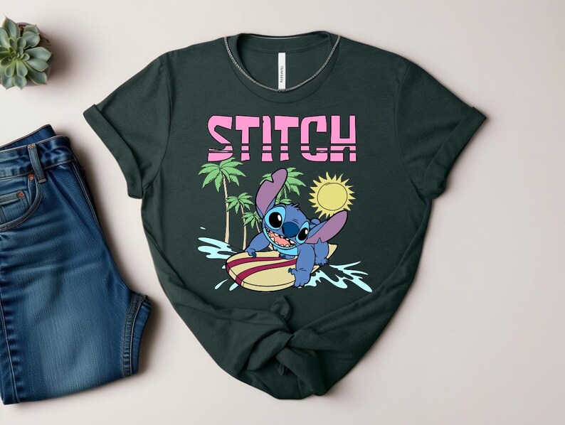 May include: Dark green t-shirt featuring the word "STITCH" in pink block letters above a cartoon character surfing. The character is blue with large ears and is riding a yellow and red surfboard. Palm trees and a sun are also in the design.