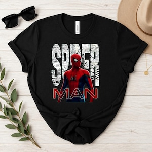 Peut inclure: Un t-shirt noir &agrave; manches courtes avec un graphisme du personnage Spider-Man dans un costume rouge et bleu. Le texte SPIDER-MAN est imprim&eacute; en grandes lettres blanches et rouges sur un fond de panneaux de bande dessin&eacute;e en noir et blanc.
