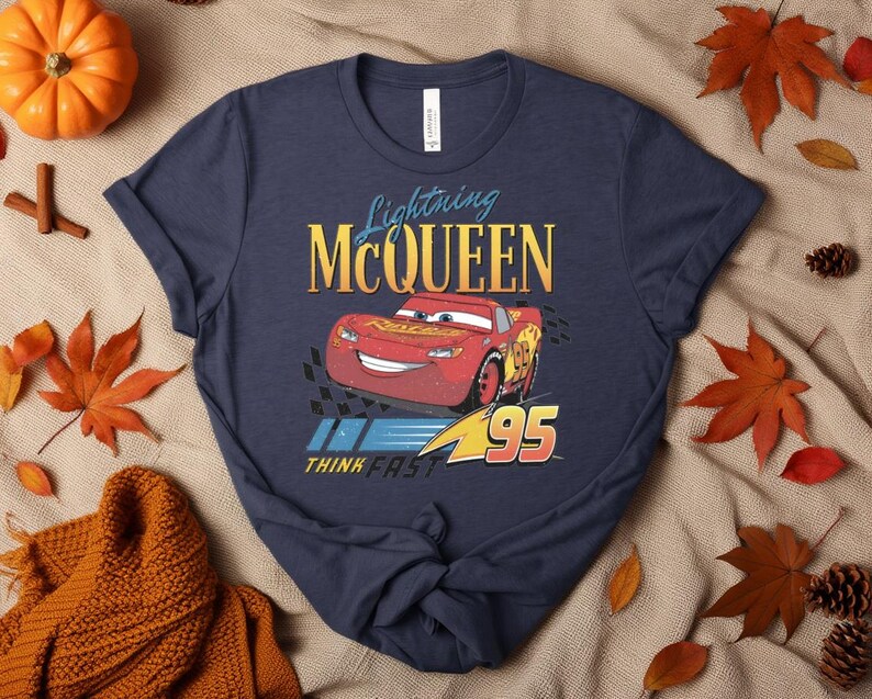 May include: Navy blue t-shirt with a graphic of Lightning McQueen from the Cars film. The design includes McQueen, the number 95, and the text "Lightning McQueen" and "Think Fast" in yellow and blue.